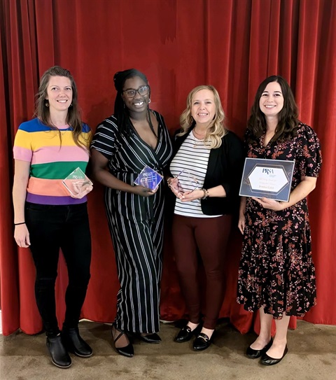 Four women are holding up trophies and a certificate