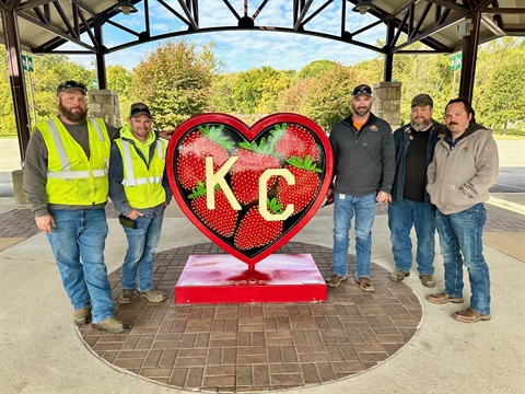 Five guys stand around a strawberry heart sculpture